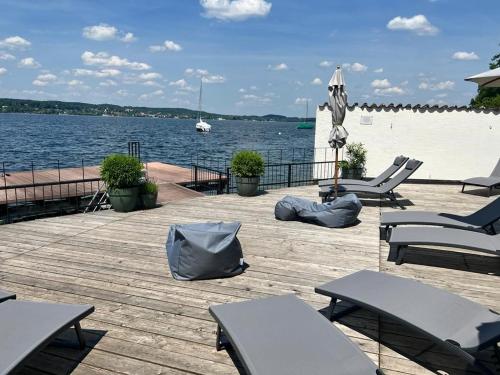 a dock with chairs and an umbrella and water at Strandhotel Berg in Berg am Starnberger See