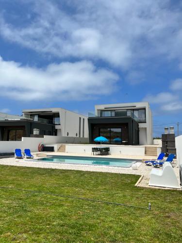 a house with a swimming pool and some blue chairs at Luxury villas with heated pool & panoramic ocean & valley views in São Martinho do Porto