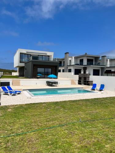 a house with a swimming pool and two blue chairs at Luxury villas with heated pool & panoramic ocean & valley views in São Martinho do Porto