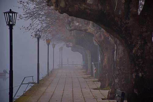 a foggy street with lights on the side of a bridge at Kasoni Home , Απόλυτα κεντρικό διαμέρισμα μπροστά στη λίμνη in Kastoria