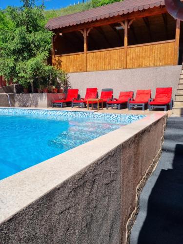 - une piscine avec des chaises rouges à côté d'un bâtiment dans l'établissement Vila Mario, à Galaţi