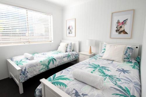 a white bedroom with two beds and a window at Callie Beach Escape - Beachside View, Family Friendly, Walk Everywhere in Caloundra