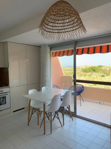 a kitchen with a white table and chairs and a balcony at Mon Petit Paradis, vue sur dunes et mer, accès direct plage Robinson, terrasse, WIFI, parking privé, très ressourçant, à Marseillan Plage in Marseillan