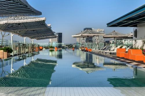 a pool of water with orange chairs and buildings at Publica Isrotel, Autograph Collection in Herzelia 
