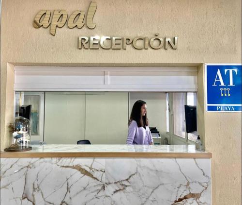 a woman is standing in front of an office at Apartamentos Apal Chinasol in Almuñécar