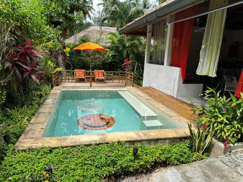 a pool with a table and an umbrella next to a house at SandShine Village in Srithanu