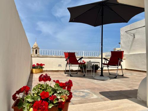 a patio with two chairs and an umbrella and flowers at The Knight - Historical terraced house overlooking the central square in Birgu