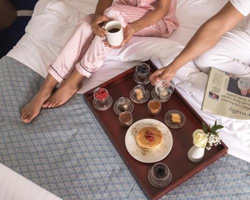 une personne assise sur un lit avec un plateau de nourriture dans l'établissement Jeddah Marriott Hotel Madinah Road, à Djeddah