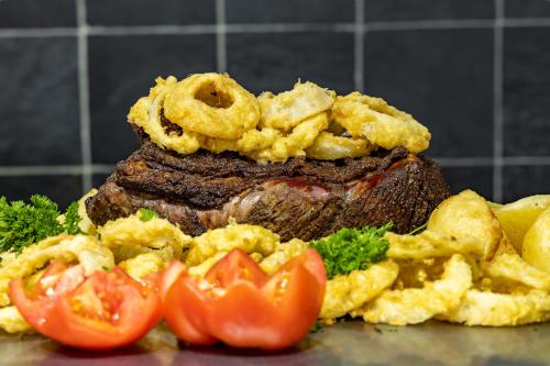 a pile of food with a steak and some tomatoes at African Sky Harrismith Inn in Harrismith