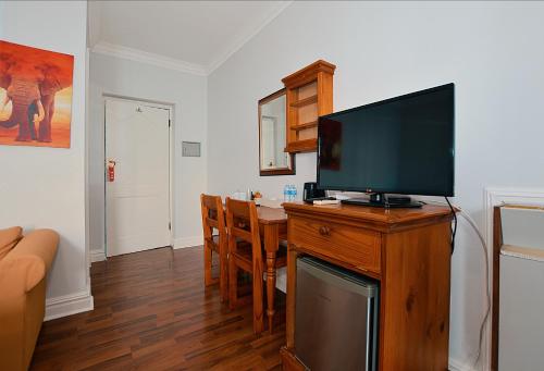 a living room with a television on a wooden stand with a dining table at Albatross Guest House Bantry Bay in Cape Town