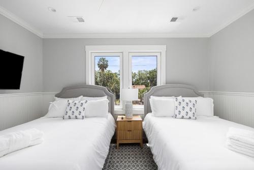 two beds in a white room with a window at The Jungle House in Edisto Island