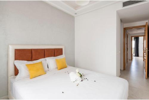 a white bedroom with a large bed with yellow pillows at Appartement 23 Ensoleillé à 5min de la Plage Piscine à 15km de l'appartement in El Jadida