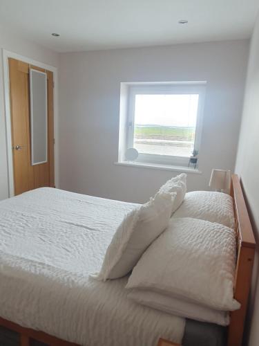 a bedroom with a bed with white sheets and a window at Self catering. Maydene. Holm. Orkney, Scotland. in Nether Button