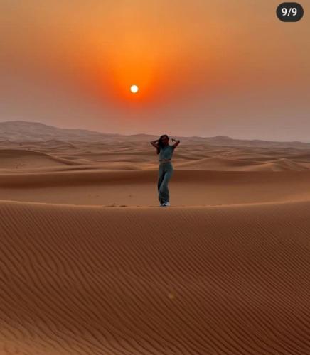a woman standing in the desert at sunset at Merzouga Top Luxury Camp in Merzouga