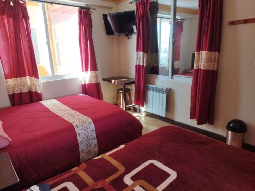 two beds in a room with red curtains and a tv at Uyuni HOSTAL YOKOSO in Uyuni