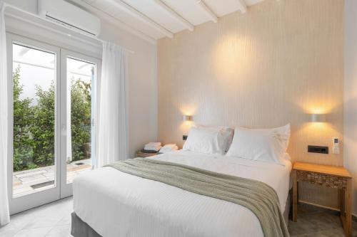 オルノスにあるIvi Mykonean Suites Mimoza Ornos Beachの白いベッドルーム(大型ベッド1台、窓付)