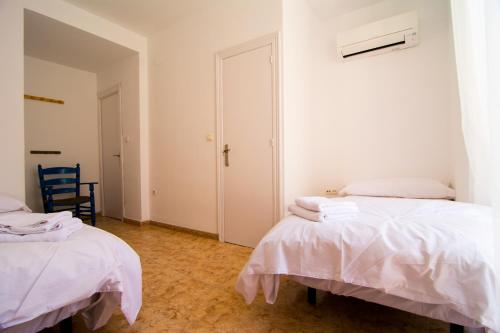 a white room with two beds and a chair at San José Guest House in Granada