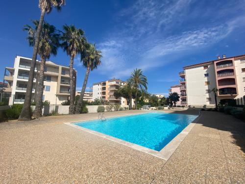 a swimming pool with palm trees and buildings at La Palmeraie 2 chambres in Sainte-Maxime
