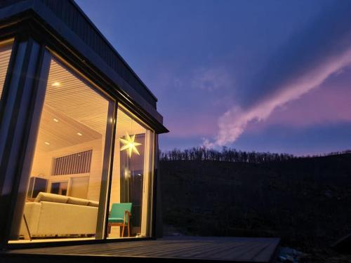 a glass house with a couch and chairs on a deck at Senjavista, near nature, sea and mighty mountains in Skaland