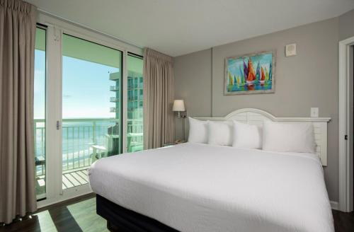 a bedroom with a large white bed and a balcony at Avista Resort in Myrtle Beach