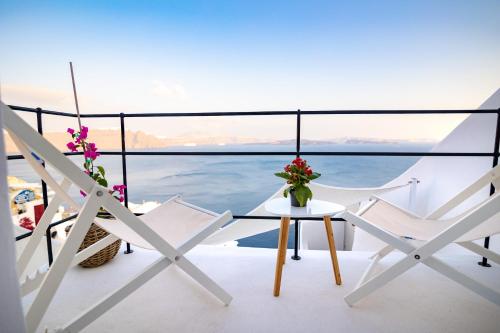 a balcony with white chairs and a table with flowers at Oia Mare Villas in Oia