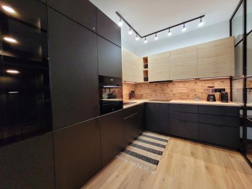 a kitchen with black cabinets and wooden floors at Ukiel Park 21 by RENT4YOU in Olsztyn