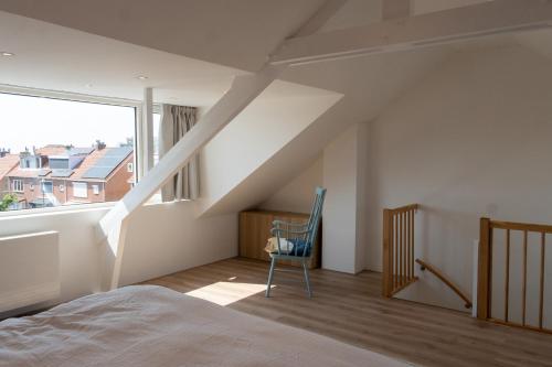 a bedroom with a bed and a chair and a window at Appartement aan Zee in Noordwijk