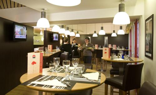 a restaurant with people sitting at tables in a restaurant at Hotel Mermoz Paris Le Bourget in La Courneuve