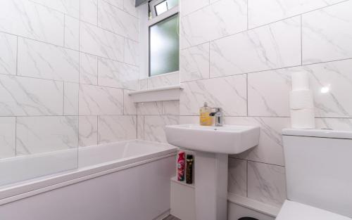 a white bathroom with a sink and a bath tub at 4 Bedrooms Homely House - Sleeps 6 Comfortably with 6 Double Beds,Glasgow, Free Street Parking, Business Travellers, Contractors, & Holiday-Goers, Near All Major Transport Links in Glasgow & City Centre, Perfect for Common Wealth Games 2026 in Glasgow