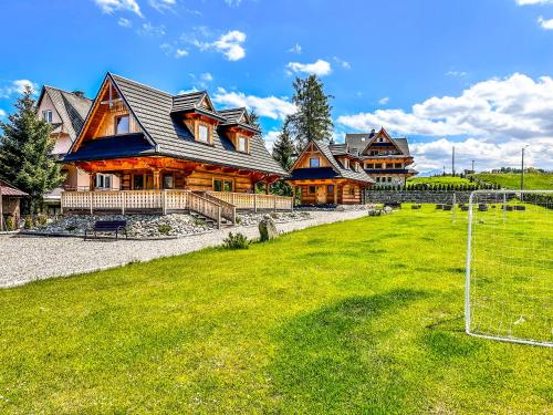 une grande maison en bois avec un terrain de football en face dans l'établissement Chaty Misiagi, à Poronin