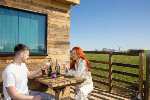 Ein Mann und eine Frau sitzen an einem Tisch mit Weinflaschen. in der Unterkunft 'Cinnabar Nest' Remote Off-Grid Eco Cabin in Sedgefield