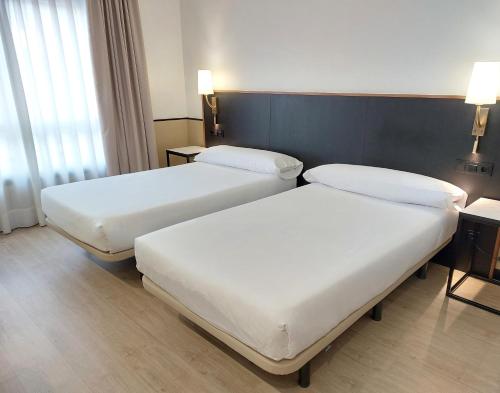 two beds in a hotel room with white sheets at Hotel Costa Atlántica in Arteixo