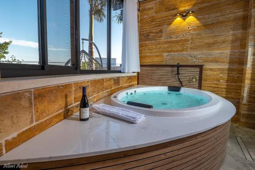 哈德奈斯的住宿－פסגת חד נס - סוויטות יוקרה，窗户旁的热水浴缸,配有一瓶葡萄酒
