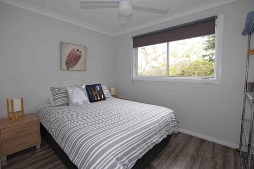 um quarto branco com uma cama e uma janela em Magnolia Cottage em Coffs Harbour