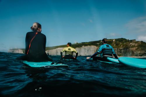 three people sitting on surfboards in the water at Gijon Surf Hostel in Gijón