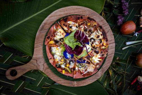 a pizza on a wooden plate on a table at Amanuba Ersadeva Resort in Pulukan