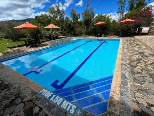 a swimming pool with blue water and orange umbrellas at La Villa de San Sebastian Hotel in Villa de Leyva