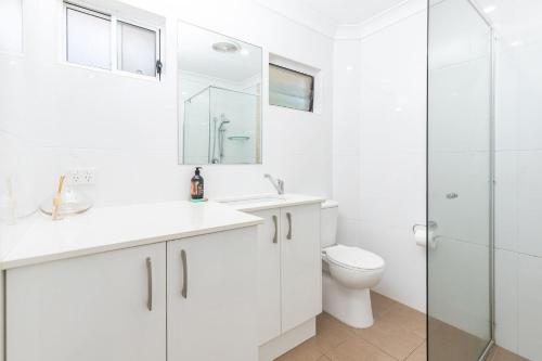 a white bathroom with a toilet and a glass shower at Boomerang Point Apartment in Blueys Beach