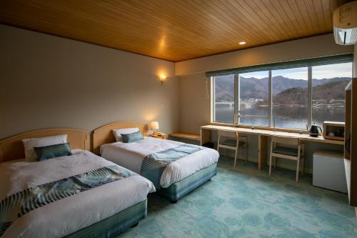 a bedroom with two beds and a desk and a window at Fuji Lake Hotel in Fujikawaguchiko