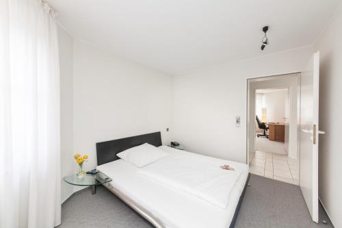 a white bedroom with a bed and a glass table at Novum Hotel Strijewski - Apartments in Wolfsburg