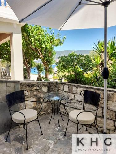 フィスカルドにあるSeaside ground floor elegant Suite in Fiskardo! 20 steps from Zavalata beach!のパティオ(椅子2脚、テーブル、パラソル付)