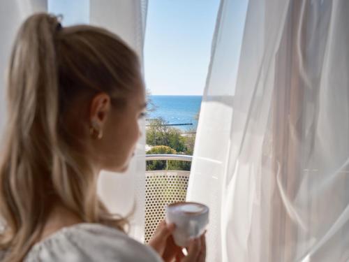 a woman holding a glass of wine looking out a window at Arka Medical Spa in Kołobrzeg