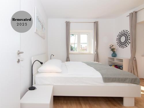 biała sypialnia z łóżkiem i oknem w obiekcie Walls of Piran Apartments and Rooms w mieście Piran