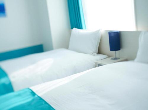 a bedroom with two beds and a blue lamp on a table at DEL style Osaka Shin Umeda by Daiwa Roynet Hotel in Osaka