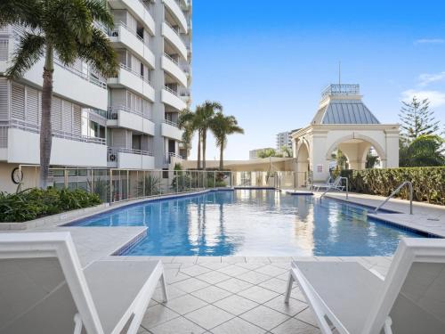 a swimming pool with two chairs and a building at Couture Comfort - Luxe Chanel Themed Apartment in Gold Coast