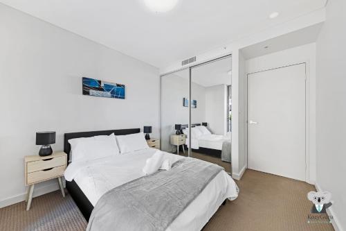 a white bedroom with a large bed and a mirror at KozyGuru / Parramatta / APT / NPA008 in Sydney