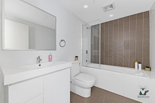 a white bathroom with a toilet and a sink and a tub at KozyGuru / Parramatta / APT / NPA008 in Sydney