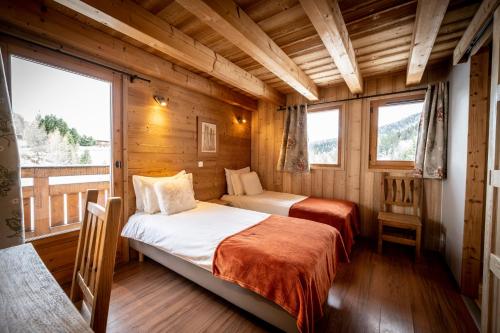 two beds in a room with wooden walls and windows at Les Chalets du Cocoon in La Plagne