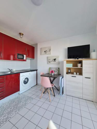 une cuisine avec des armoires rouges et une table avec une chaise rose dans l'établissement Appartement EN PREMIÈRE LIGNE DE PLAGE HENDAYE, à Hendaye