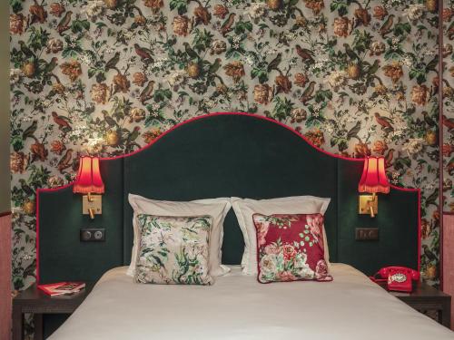 uma cama com duas almofadas num quarto com papel de parede floral em Hôtel Brittany em Paris
